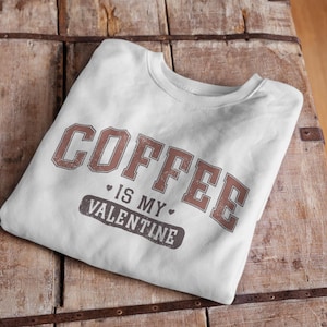 Può includere: Felpa bianca con testo marrone che dice "Coffee is my Valentine".