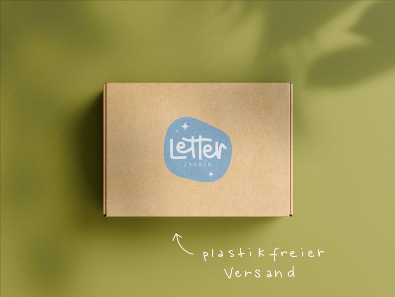 May include: A brown cardboard box with a blue logo reading "Letter Zauber" on a green background. The box has a handwritten arrow pointing to the text "plastic free shipping".