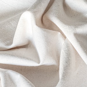 May include: A close-up of a white fabric with a textured surface. The fabric is folded and wrinkled, creating a soft and natural look.
