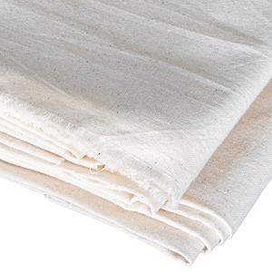 May include: A stack of white cotton fabric with a raw edge. The fabric is folded in half and the edges are visible.