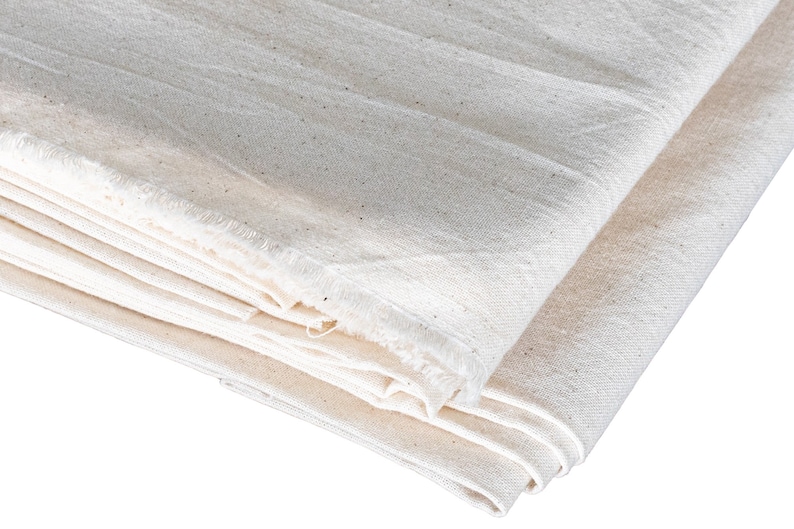 May include: A stack of white cotton fabric with a raw edge. The fabric is folded in half and the edges are visible.
