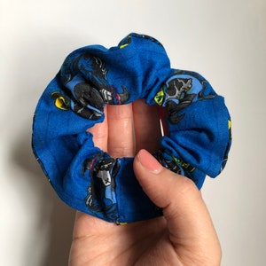 May include: Blue fabric scrunchie with a black and yellow print of a cartoon character.