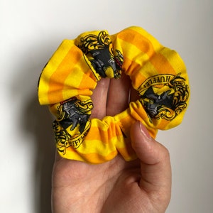 May include: Yellow and black scrunchie with a Hufflepuff crest and the words "Hufflepuff" printed on it.