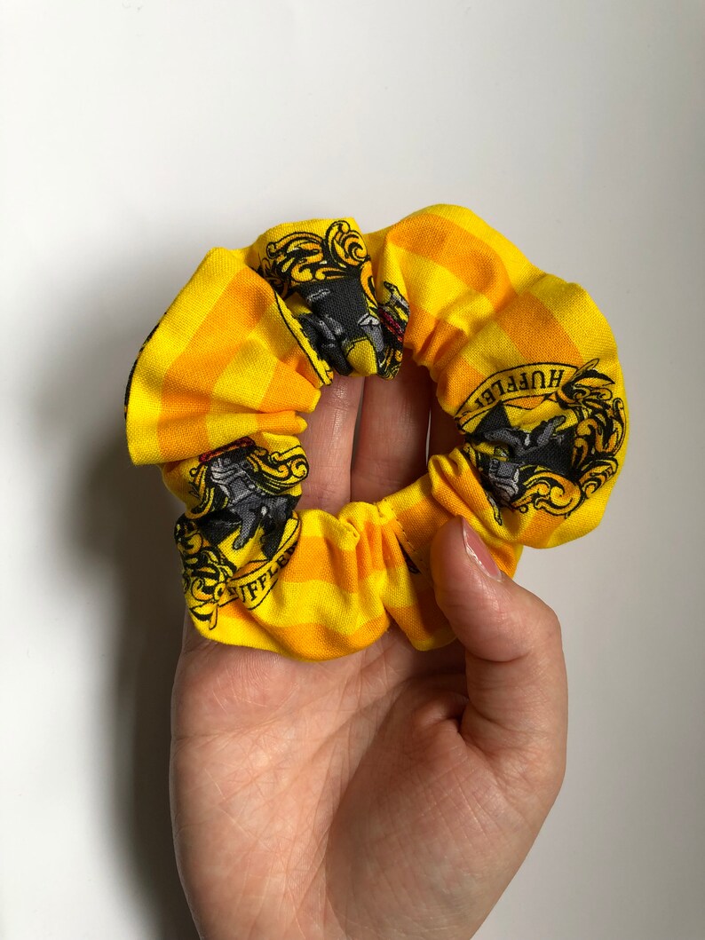 May include: Yellow and black scrunchie with a Hufflepuff crest and the words "Hufflepuff" printed on it.