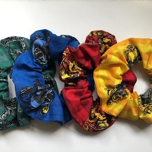 May include: Four fabric hair scrunchies with different Hogwarts house crests. The scrunchies are green, blue, red, and yellow.