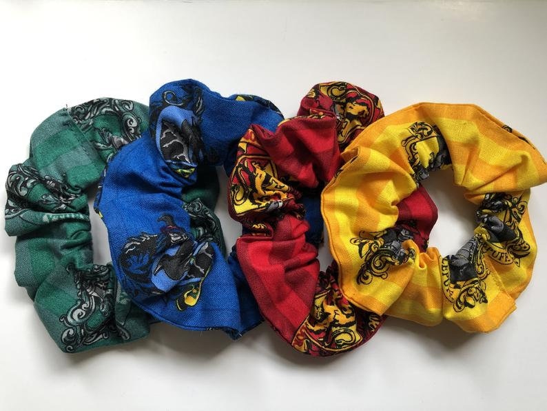 May include: Four fabric hair scrunchies with different Hogwarts house crests. The scrunchies are green, blue, red, and yellow.