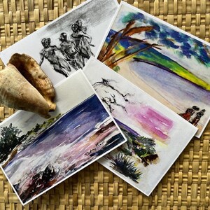 Könnte beinhalten: Eine Sammlung von Aquarelldrucken mit Küstenlandschaften und abstrakten Figuren, zusammen mit zwei Muscheln. Die Drucke zeigen eine Vielzahl von Farben, darunter Blau-, Grün- und Lilatöne, angeordnet auf einer gewebten Oberfläche.