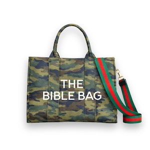May include: A camouflage-patterned tote bag with the text "THE BIBLE BAG" in white. The bag has a green and red striped shoulder strap and matching handles. The bag is designed for carrying items.