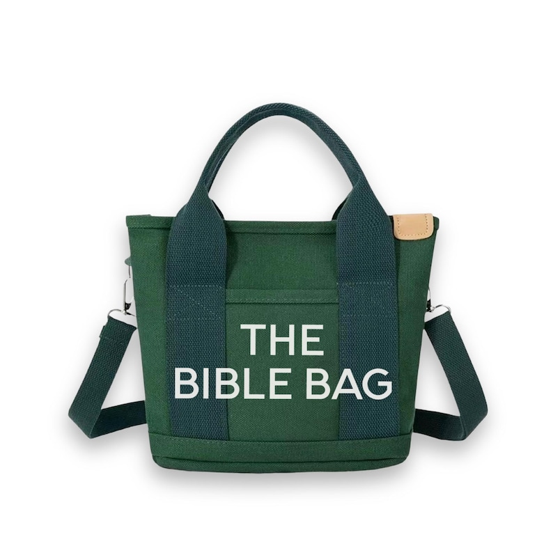 May include: A green canvas tote bag with the text "THE BIBLE BAG" in white. The bag has a top handle and a detachable shoulder strap. A small tan leather patch is on the top right corner.