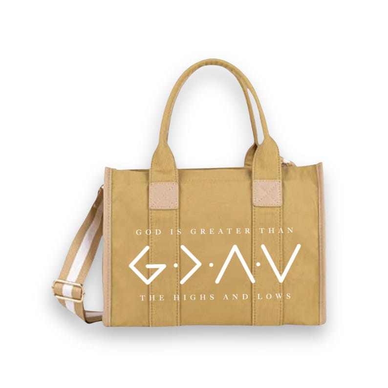 May include: A mustard yellow canvas tote bag with two top handles and a detachable shoulder strap. The front features white text that reads "GOD IS GREATER THAN THE HIGHS AND LOWS" alongside the G>&Lambda;V symbol in a clean, modern white font.