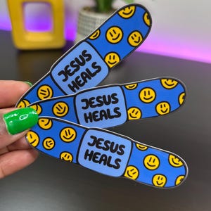 May include: Three blue and yellow band-aid stickers with the text "Jesus Heals" on each one. The band-aids are decorated with yellow smiley faces.