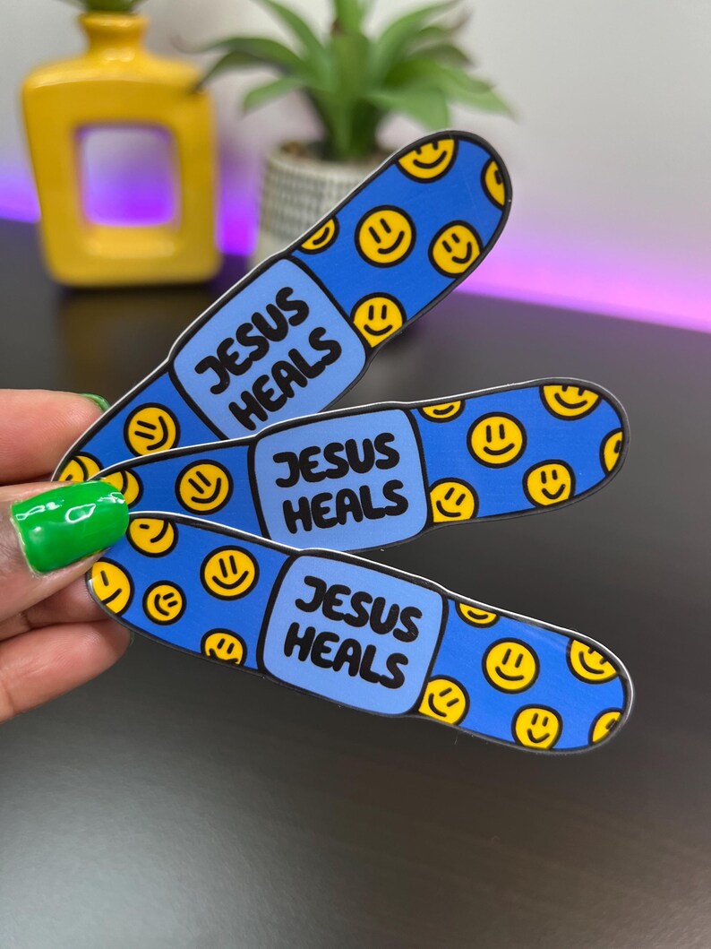 May include: Three blue and yellow band-aid stickers with the text "Jesus Heals" on each one. The band-aids are decorated with yellow smiley faces.