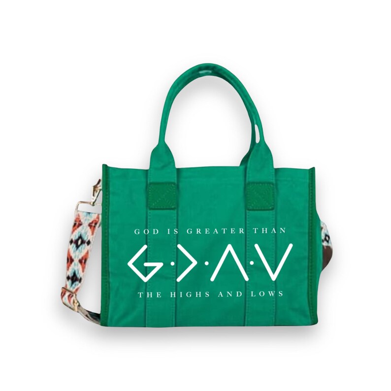 May include: A bright green canvas tote bag with two top handles and a detachable patterned shoulder strap. The front features white text reading GOD IS GREATER THAN THE HIGHS AND LOWS, accompanied by the corresponding mathematical symbols.