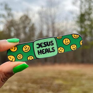 May include: Green band-aid sticker with a smiley face pattern and the text "JESUS HEALS" in black.