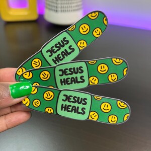 May include: Three green and yellow band-aid stickers with the text "Jesus Heals" on each one. The band-aids are covered in yellow smiley faces.