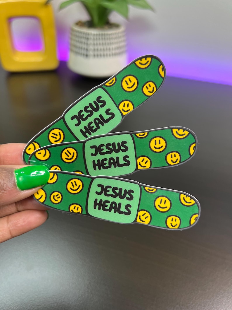 May include: Three green and yellow band-aid stickers with the text "Jesus Heals" on each one. The band-aids are covered in yellow smiley faces.