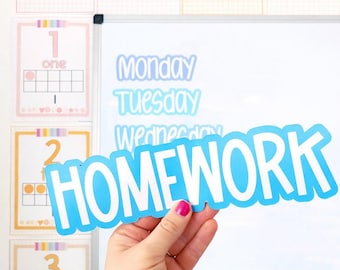 May include: A hand holds a blue "HOMEWORK" sign in front of a whiteboard with the days of the week written on it. Above are alphabet cards and number cards. The cards have a pink, yellow, and orange color scheme.