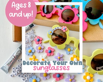 May include: A craft kit for decorating your own sunglasses. The kit includes a pair of yellow sunglasses with flower-shaped frames, a variety of colorful flower embellishments, and a tube of glue. The sunglasses are decorated with the word "ADDI" in white letters. The kit is suitable for ages 8 and up.