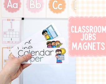 May include: A hand holding classroom job magnets with illustrations of children and the words "Line", "Calendar", and "Paper". The image also shows a pink sign that says "Classroom Jobs Magnets". Background includes alphabet and number charts.