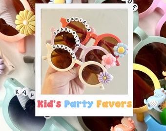 May include: A collection of colorful round sunglasses with personalized names, such as "Caprice", "Charlotte", "Daniella", and "Wade", decorated with colorful flowers. Kid's Party Favors is written in a colorful font at the bottom of the image.