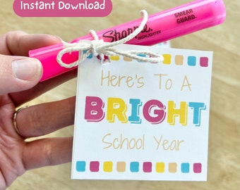 May include: A pink highlighter with a white tag tied around it. The tag has the text "Here's To A BRIGHT School Year" in colorful letters.