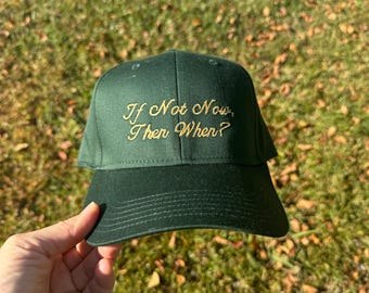 May include: A dark green baseball cap with the text "If Not Now, Then When?" embroidered in gold on the front.