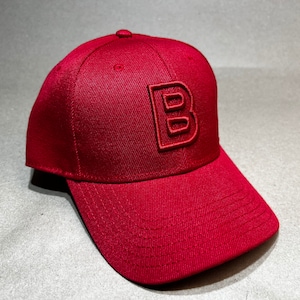 Puede incluir: Una gorra de béisbol roja con una gran letra "B" bordada en relieve en la parte delantera.