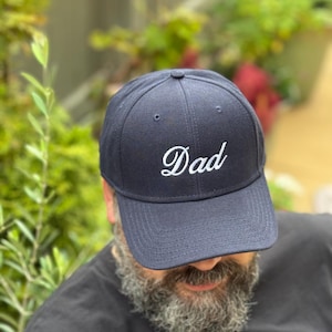 May include: A navy blue baseball cap with a white embroidered "Dad" on the front.