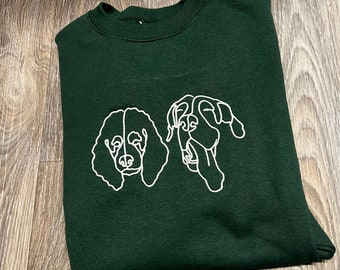 May include: A dark green sweatshirt with a white outline of two dog heads. The dog on the left has curly hair and the dog on the right has floppy ears.