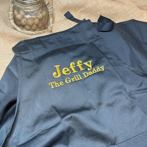May include: Black apron with the text "Jeff The Grill Daddy" embroidered in gold thread.