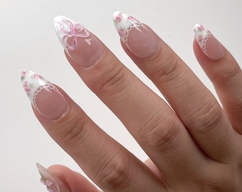 Puede incluir: Primer plano de una mano con cinco uñas pintadas con una base blanca y diseños florales rosas.