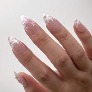 May include: Close-up of a hand with five nails painted with a white base and pink floral designs.
