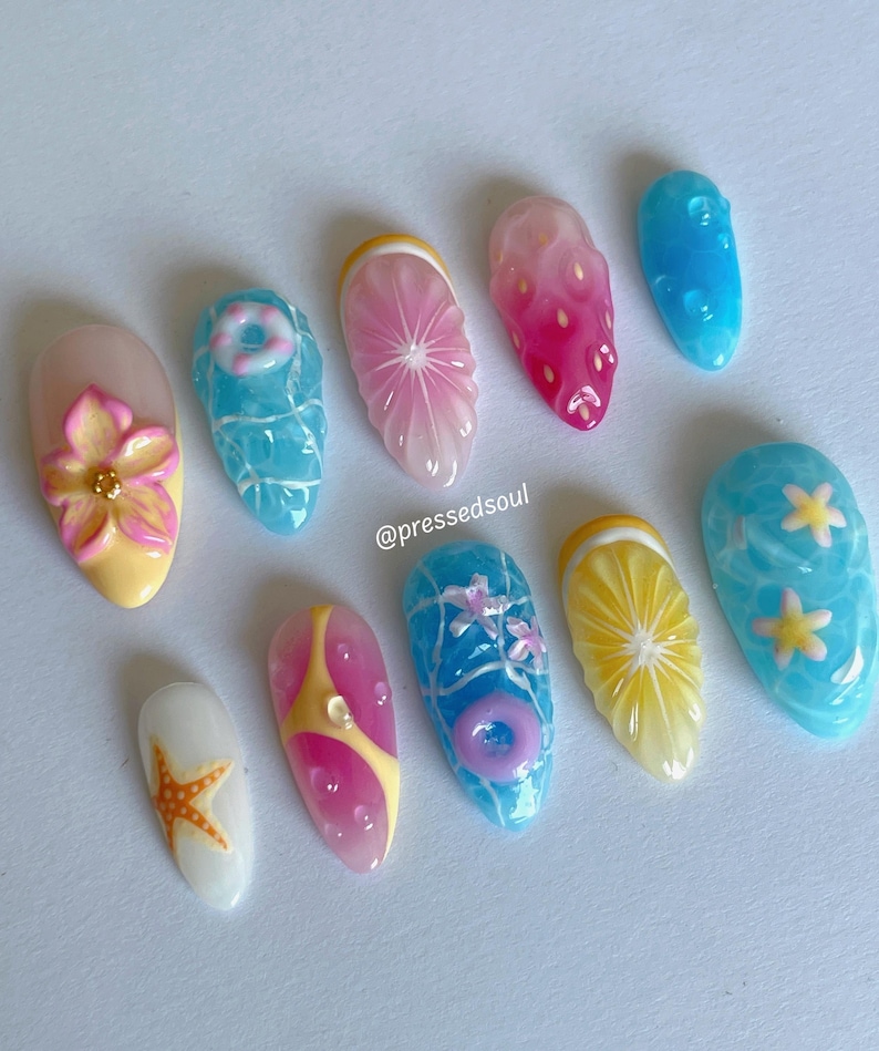 Pu&ograve; includere: Una collezione di dieci unghie acriliche con disegni a tema estivo. Le unghie presentano vari disegni, tra cui un fiore, una stella marina, un salvagente e fette di frutta. I colori includono rosa, giallo, blu e bianco. Le unghie sono disposte su una superficie bianca.