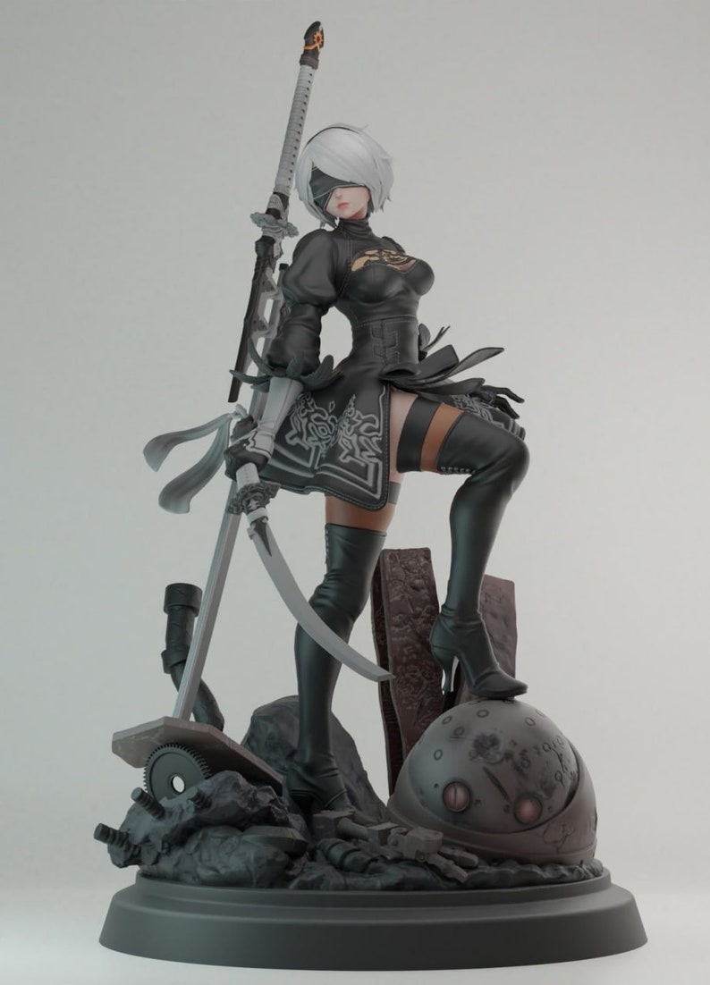 Op de afbeelding: Een zwart-wit figuur van een vrouwelijk personage met een zwaard, staand op een ronde basis met een metalen bol. Het figuur draagt een zwarte jurk en laarzen en heeft een wit ooglapje over haar ogen.