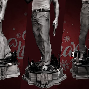 May include: A gray and white figurine of a man holding two guns, standing on a base with the words "Die Hard" and "Yippee-Ki-Yay" printed on it. The base is shaped like a building with a Christmas tree on top.