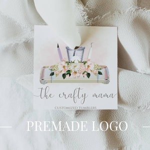 May include: A premade logo design for a business called "the crafty mama" that specializes in customized tumblers. The logo features a white background with a pink and white floral design and a tray with crafting tools. The text "the crafty mama" is written in a black script font.