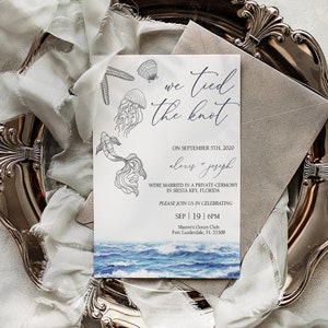 May include: A wedding invitation with a watercolor illustration of jellyfish and ocean waves. The invitation reads "We tied the knot" and includes the date, names of the couple, and details about the wedding reception. The invitation is on a silver tray with a white silk ribbon.