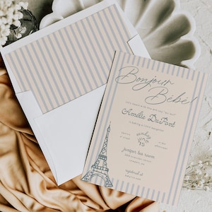 May include: A baby shower invitation with a Parisian theme. The invitation features the text "Bonjour Bébé!" and the name "Amélie Du Pont". The design includes a light blue Eiffel Tower illustration and vertical stripes.