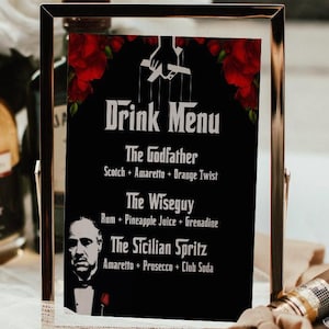 May include: A framed black drink menu with red rose accents and the words "Drink Menu" at the top. The menu lists three cocktails: The Godfather, The Wiseguy, and The Sicilian Spritz. A bottle of whiskey and a watch are in the background.