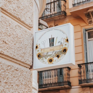 May include: A white sign with a round logo featuring sunflowers and the text "Sunshine Creations" with the tagline "Personalized Tumblers, Totes, and More".