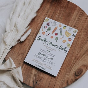 May include: A white card with a watercolor illustration of various fruits and vegetables. The text on the card reads "Locally Grown Baby, family owned & operated, 100% organic". The card also includes the text "Please Join Us For A Baby Shower In Honor Of The Parents To Be, Samantha & Carter, Saturday, March 20, 2020, 2-5 PM, 231 Garden St. Boulder, CO 12345, RSVP to Samantha by 3/1 555-555-5555, registered at Target".
