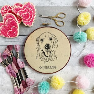 Op de afbeelding: Een beige borduurring met een zwart-witte lijntekening van een golden retriever. De naam van de hond, "Duncan", is onder de afbeelding geborduurd. De ring is omgeven door roze, gele en blauwe pompoenen en roze borduurgaren.