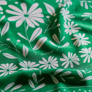 May include: Green fabric with a white floral pattern. The fabric has a subtle sheen and is folded in the center. The text "miauw" is printed in white on the fabric.