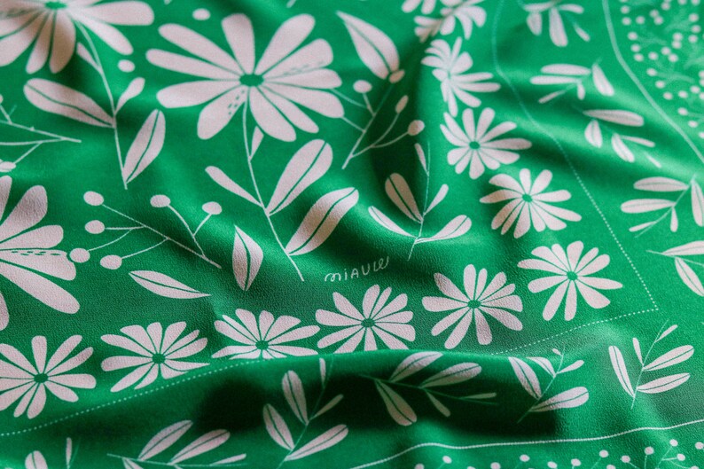 May include: Green fabric with a white floral pattern. The fabric has a subtle sheen and is folded in the center. The text "miauw" is printed in white on the fabric.