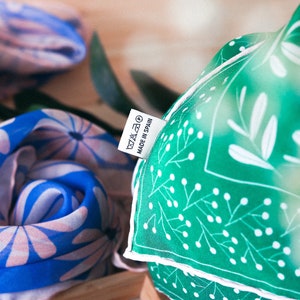 May include: Two fabric scarves with floral patterns. One scarf is blue with pink flowers and the other is green with white leaves and dots. A white tag with the text "MADE IN SPAIN" is attached to the green scarf.