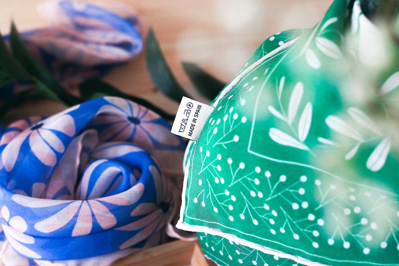 May include: Two fabric scarves with floral patterns. One scarf is blue with pink flowers and the other is green with white leaves and dots. A white tag with the text "MADE IN SPAIN" is attached to the green scarf.