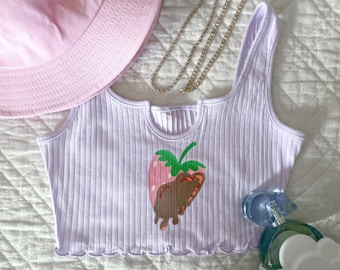 Op de afbeelding: Een lavendelkleurig geribbeld tanktop met een afbeelding van een aardbei gedoopt in chocolade. Het topje heeft een gerimpelde zoom.
