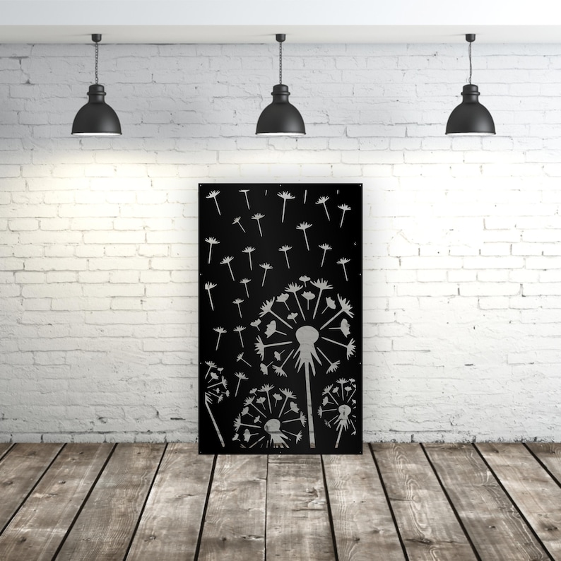 May include: A black metal wall art piece featuring a dandelion design. The artwork shows several dandelion seed heads with seeds blowing away. The piece is displayed against a white brick wall and wooden floor.