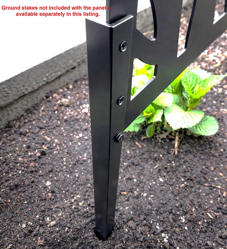 a close-up view of a black metal ground stake attached to a metal frame, with a small green plant growing next to it.