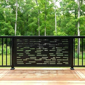 May include: Black metal deck railing with a decorative panel featuring horizontal cut-out designs. The railing is set against a backdrop of lush green trees and a wooden deck.